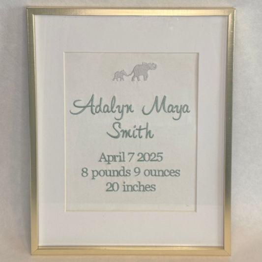 Framed embroidery with baby's name, birth date, weight, and height on a light background
